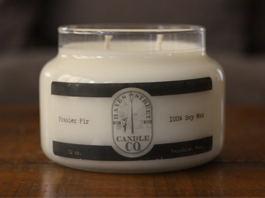 White candle in a glass jar with a black label on a wooden surface
