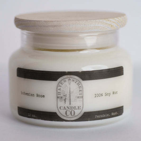 A 12 oz soy wax candle in a clear glass jar with a light wood lid, featuring a black and white label from Hayes Street Candle Co. in 'Bohemian Rose' scent.