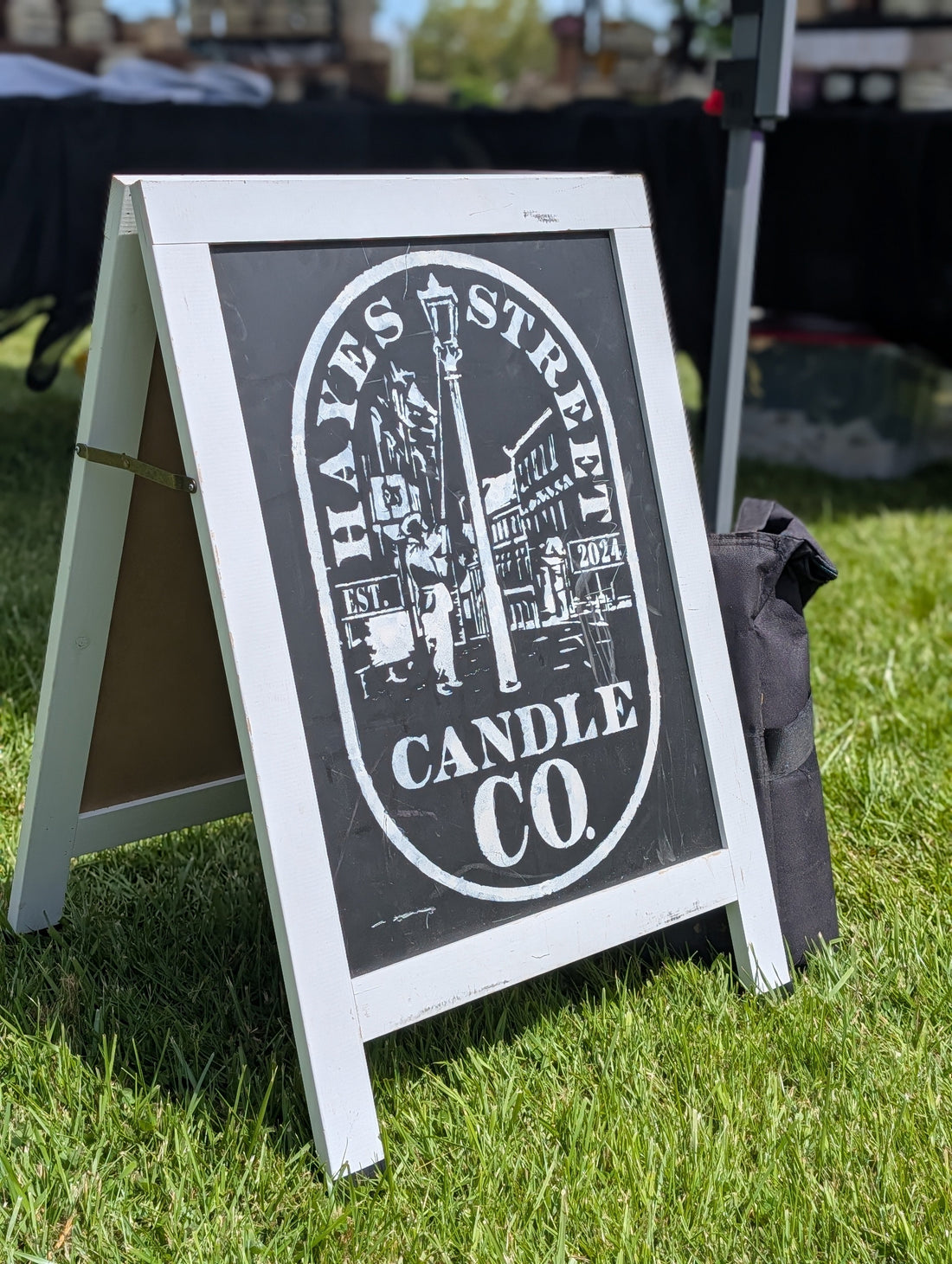 Hayes Street Candle Company sign set up on green grass. The logo is white, the background is black chalkboard, and the frame is white. It is a sunny day. Hayes Street Candle Company products are hand-poured by Margie Creen in Ferndale, Washington.