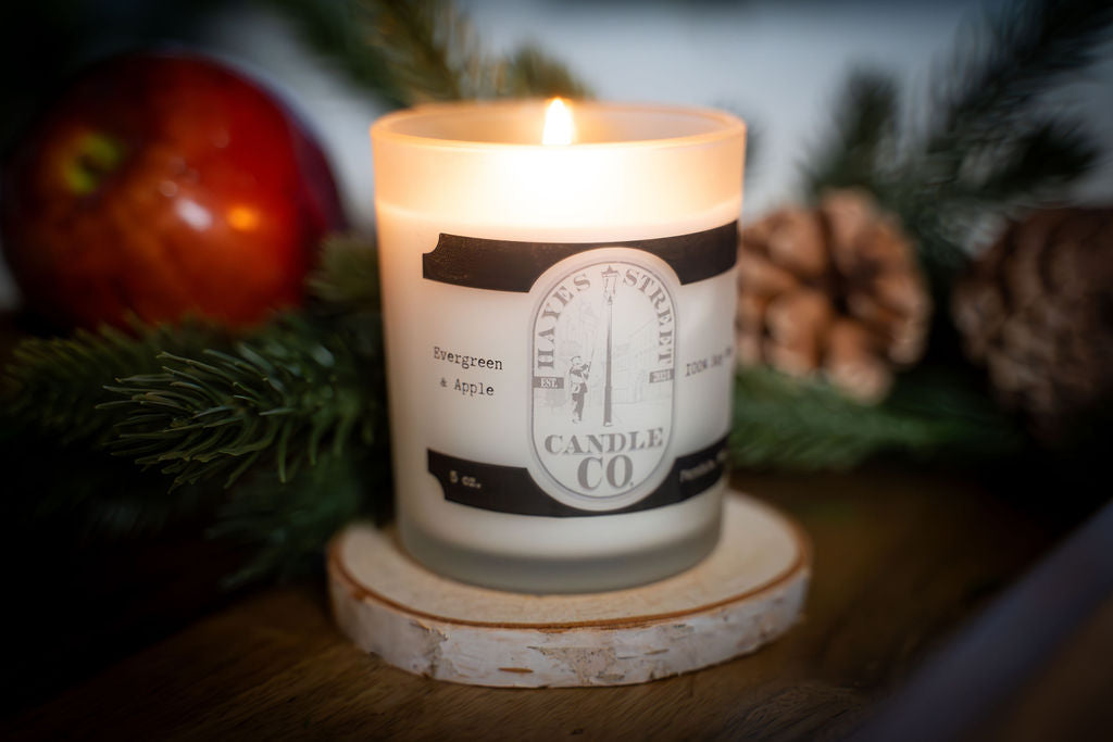 Candle with a label on a wooden coaster surrounded by Christmas decorations