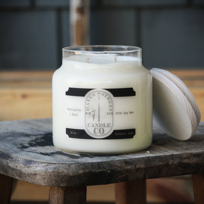 Eucalyptus and Mint soy wax candle from Hayes Street Candle Company. It is double wicked and in an apothecary-style jar with a wooden lid leaning against the side of it. This candle burns for approximately 70 hours.