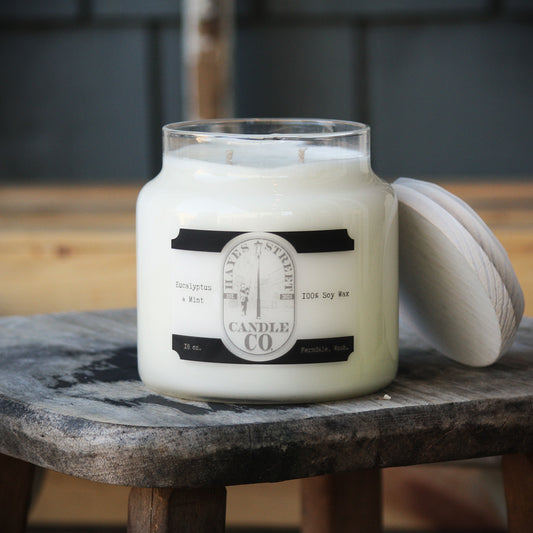 Eucalyptus and Mint soy wax candle from Hayes Street Candle Company. It is double wicked and in an apothecary-style jar with a wooden lid leaning against the side of it. This candle burns for approximately 70 hours.