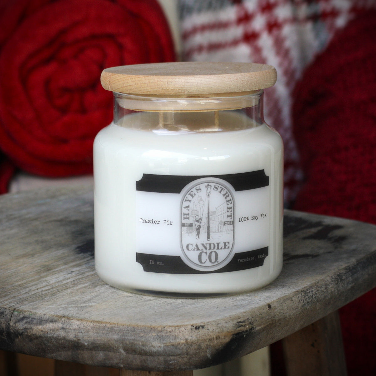 Fraser Fir candle from Hayes Street Candle Company. It is pictured with red blankets in the background on a wooden stool. Ferndale Wash