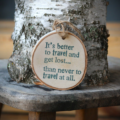 A round wooden hanging ornament with a natural wood edge and twine loop, printed with the quote "It's better to travel and get lost.... than never to travel at all." Made by Log Slices by Margie aka Hayes Street Candle Company of Ferndale, Washington, USA.