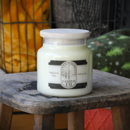 A jar candle with creamy off-white wax sits on a rustic wooden stool. The candle has a light wood lid and a black-and-white label reading 'Hayes Street Candle Co.