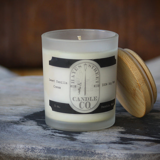 Cream-colored soy candle in a frosted glass jar with a bamboo lid resting beside it on a rustic wood surface. The label reads Hayes Street Candle Co. Ferndale Washington, 5oz 100% soy wax.
