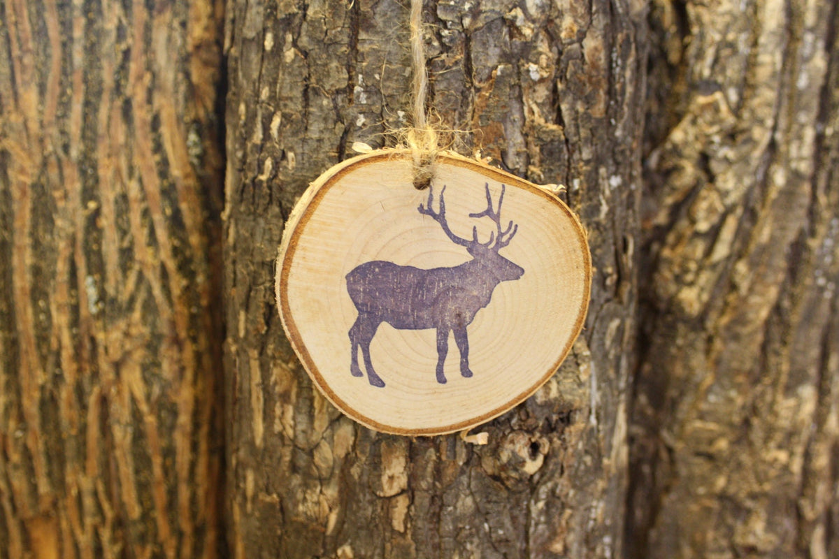 Wooden round tag with blue elk design hanging on a tree trunk