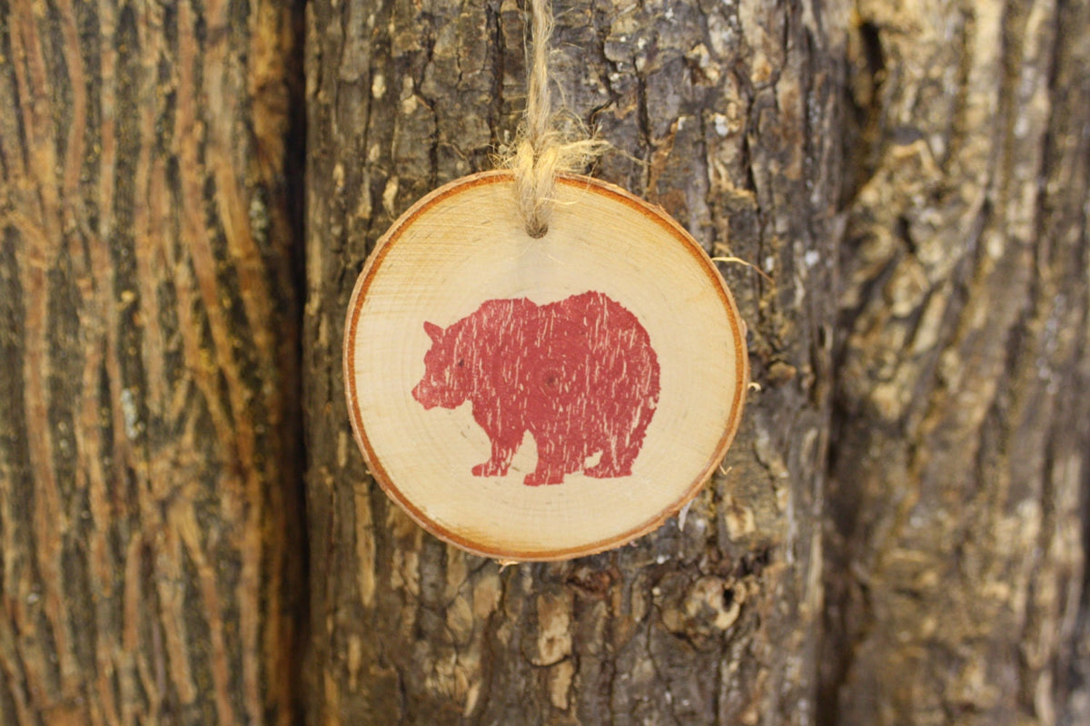 Wood birch slice ornament with red bear stamp design hanging on a tree trunk