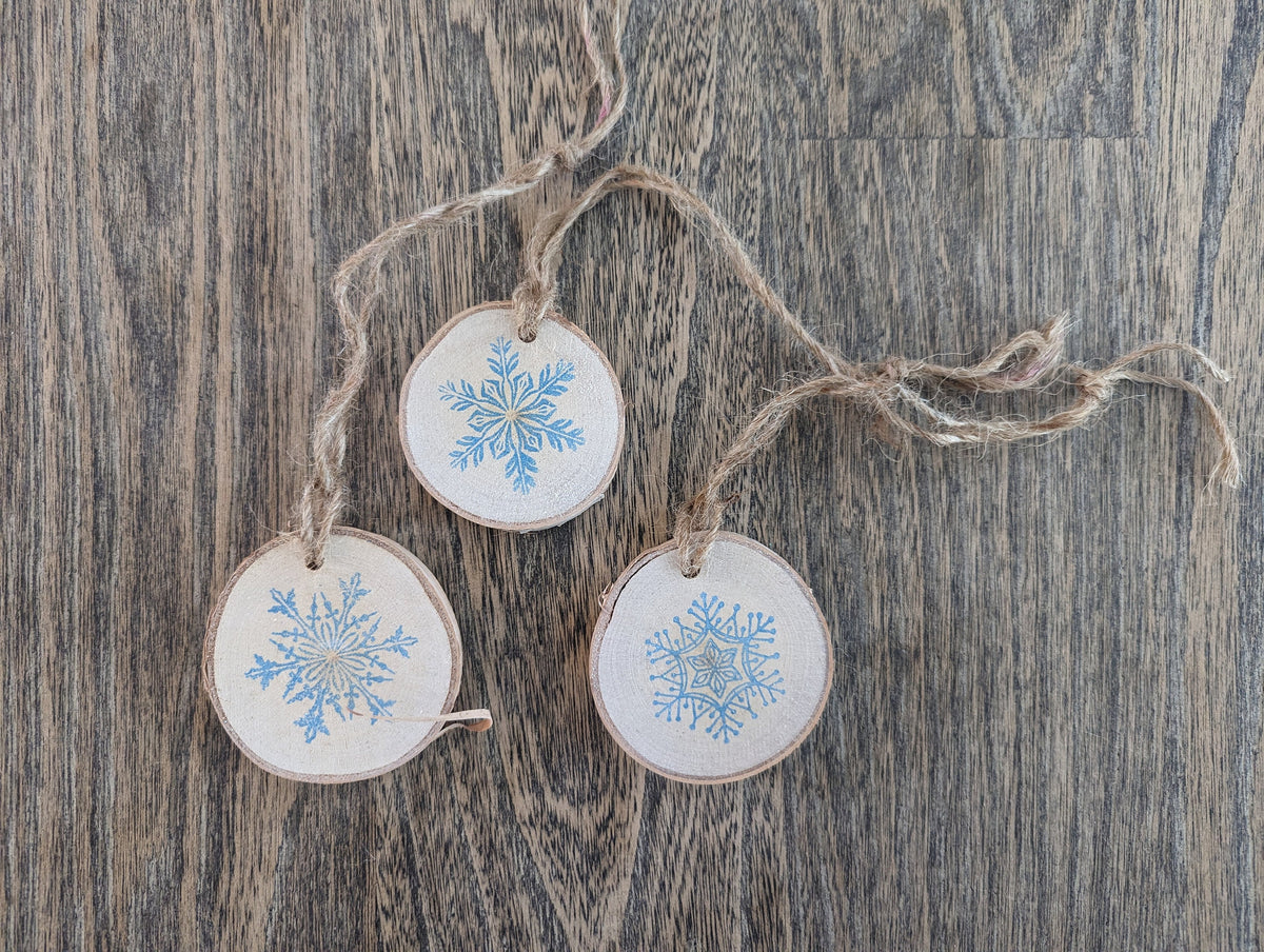 Three wooden ornaments with snowflake designs hanging on a string against a wooden background.