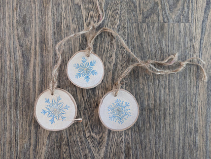 Three wooden ornaments with snowflake designs hanging on a string against a wooden background.