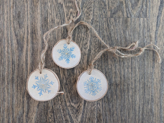 Three wooden ornaments with snowflake designs hanging on a string against a wooden background.